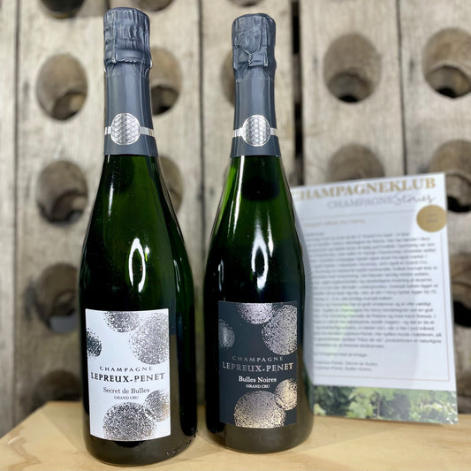 Juni 2025 klubkasse bestående af 2 flasker champagne fra Champagne Lepreux-Penet, Champagne Secret de Bulles og Bulles Noires. Klubkasseflyer og baggrund er en pupitre