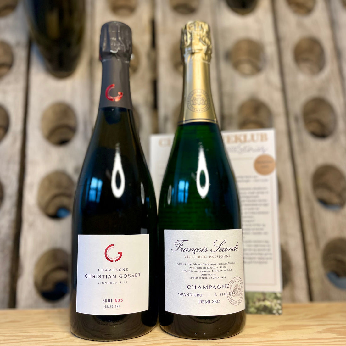 2 flasker champagne med pupitre i baggrund og klubflyer. Champagne Christian Gosset A05, Extra Brut og Champagne Francois Secondé Grand Cru, Demi-Sec
