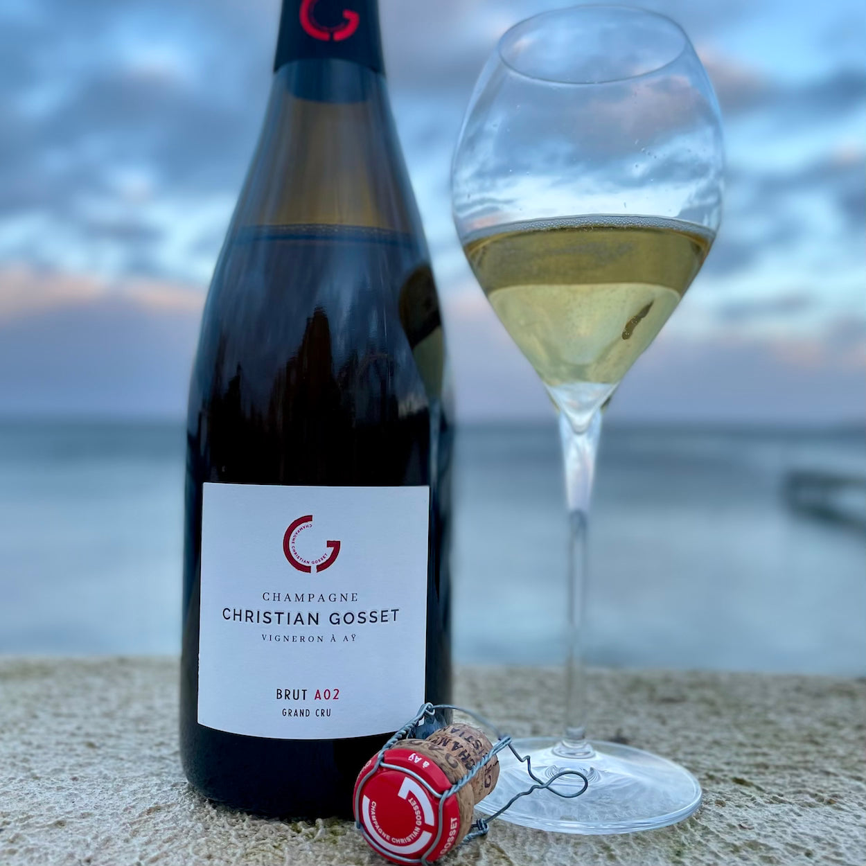 Champagne flaske og fyldt champagneglas står med udsigt til have og himmel, champagneprop, Champagne Christian Gosset Brut  A02 Grand Cru