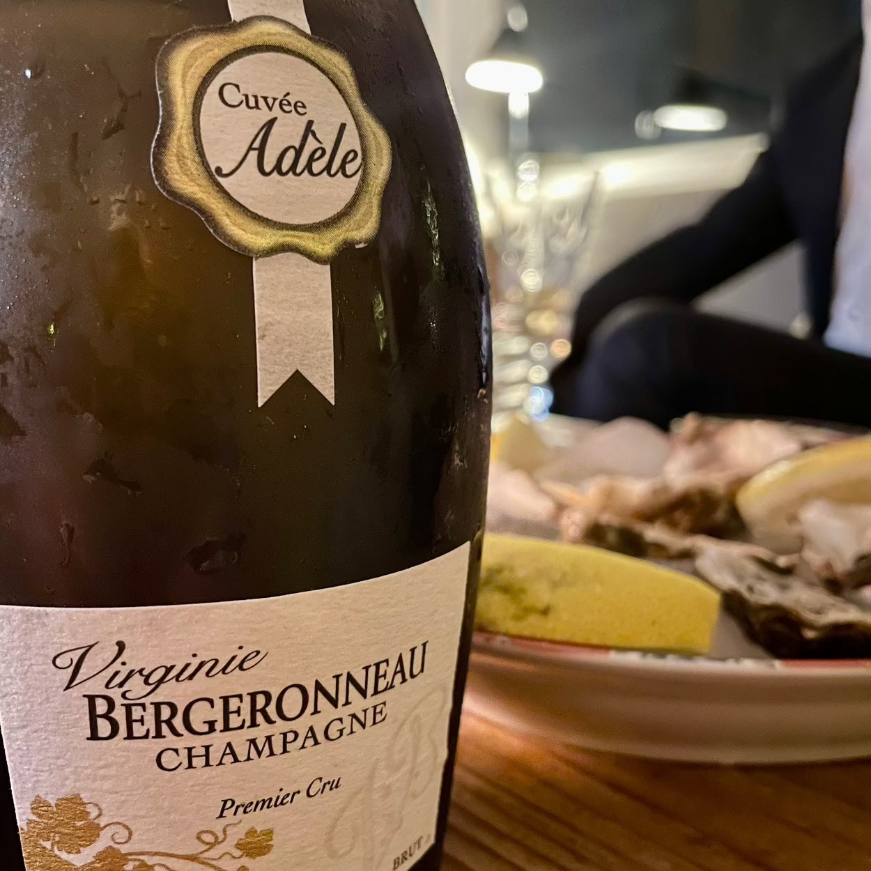 Champagne flaske tæt på, champagne Virginie Bergeronneau champagne, Premier Cru, Cuvée Adéle, Blanc de Blancs, 100% Chardonnay, brut, ved siden ses en tallerken med østers og citron skive