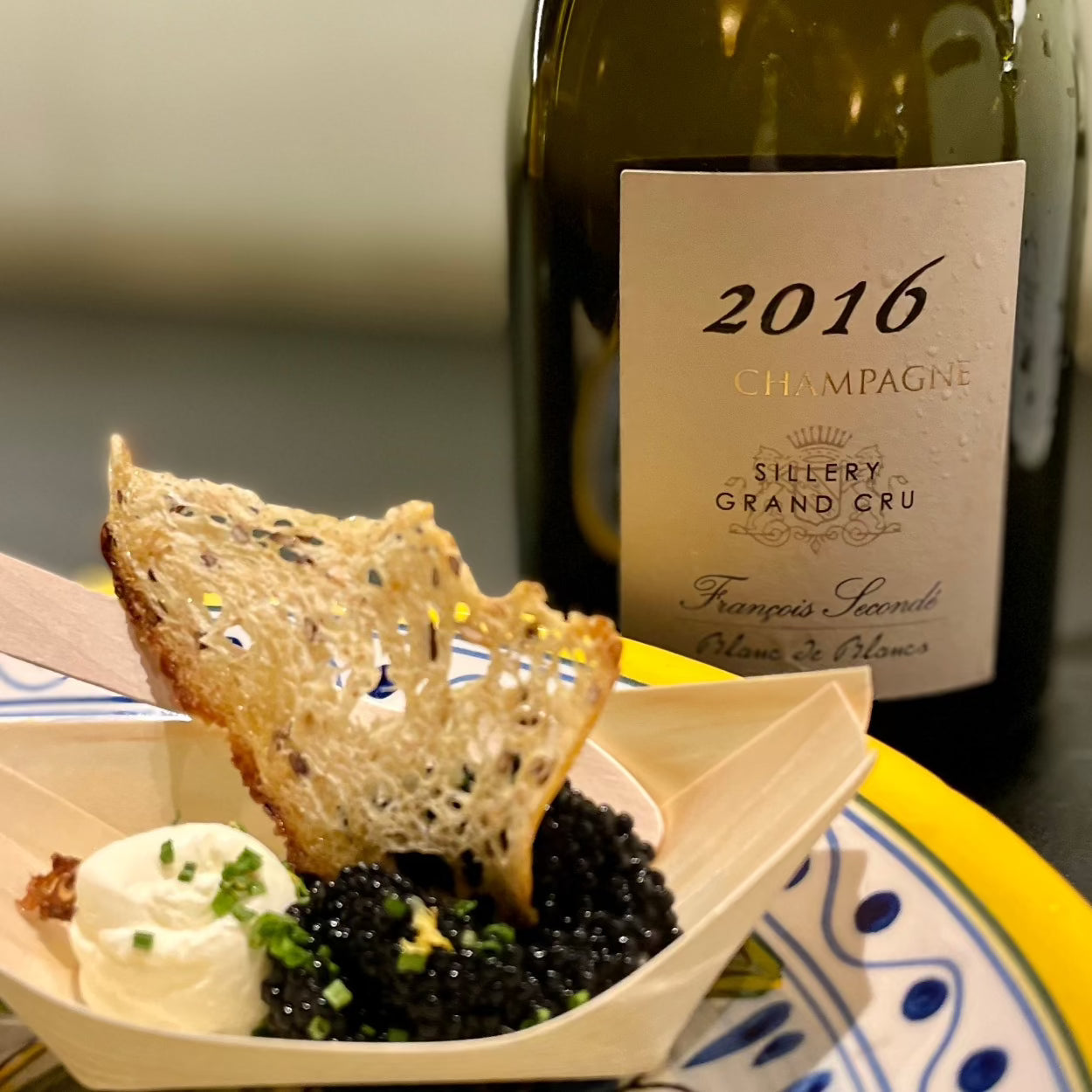 1 flaske champagne foran en tallerken med en bambus skål med sort caviar, brødskive og creme fraiche, Francois Seconde champagne, 2016, Grand Cru champagne, Blanc de Noirs, brut, årgangschampagne