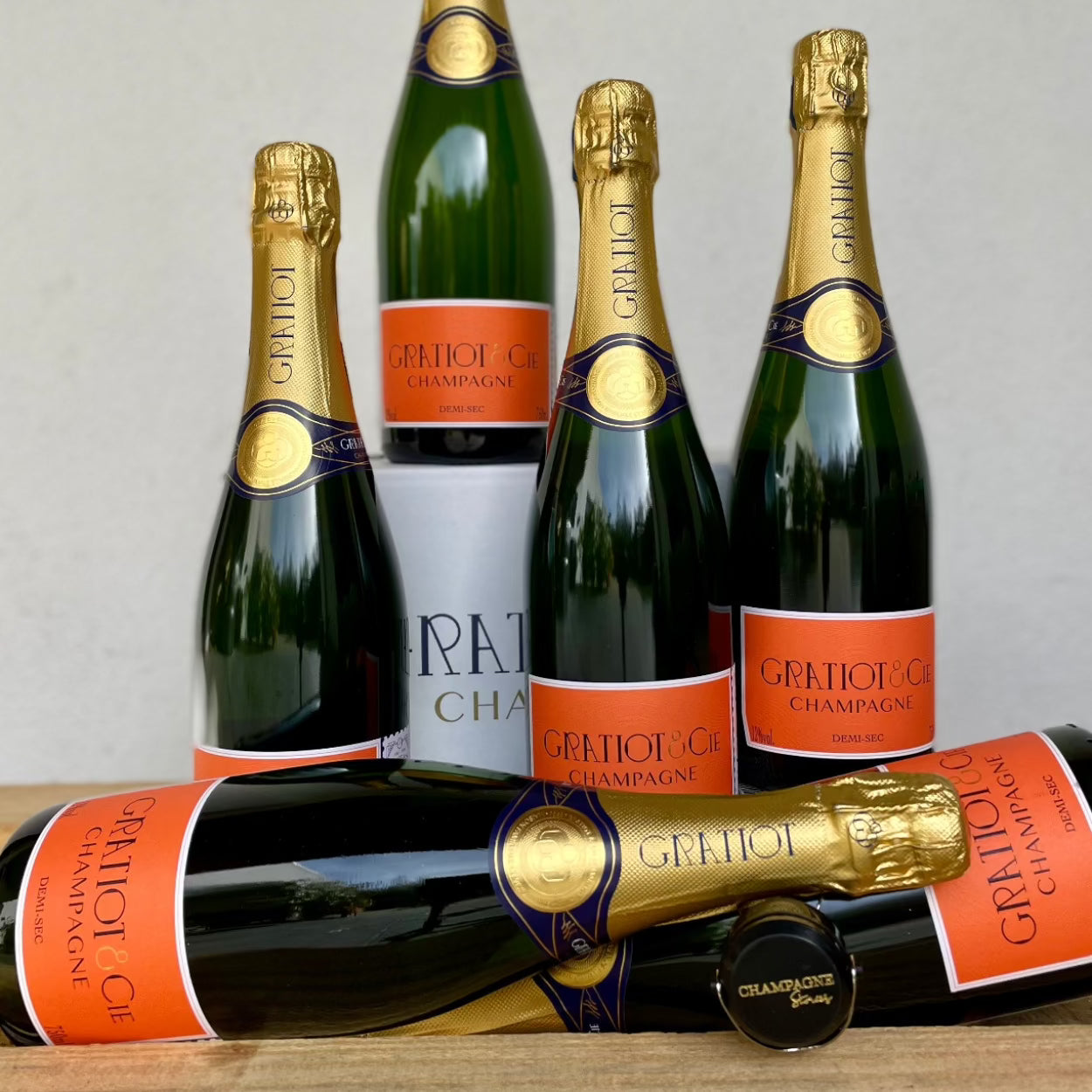 2 liggende og 4 stående flasker  champagne på hvid baggrund fra Champagne Gratiot & Cie, Demi-Sec, orange etikette, champagnestopper med logo "Champagne Stories"