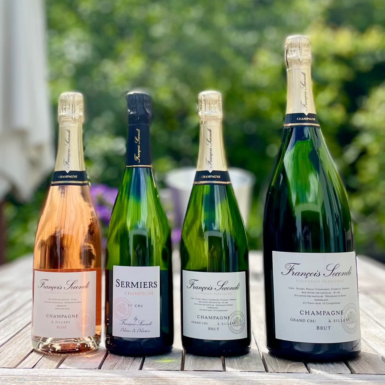 4 flasker champagne, 3 almindelige og 1 magnum flaske, Champagne Francois Seconde, Rosé, Sermiers, Brut Grand Cru og Brut Grand Cru magnum flaske på et bord i haven