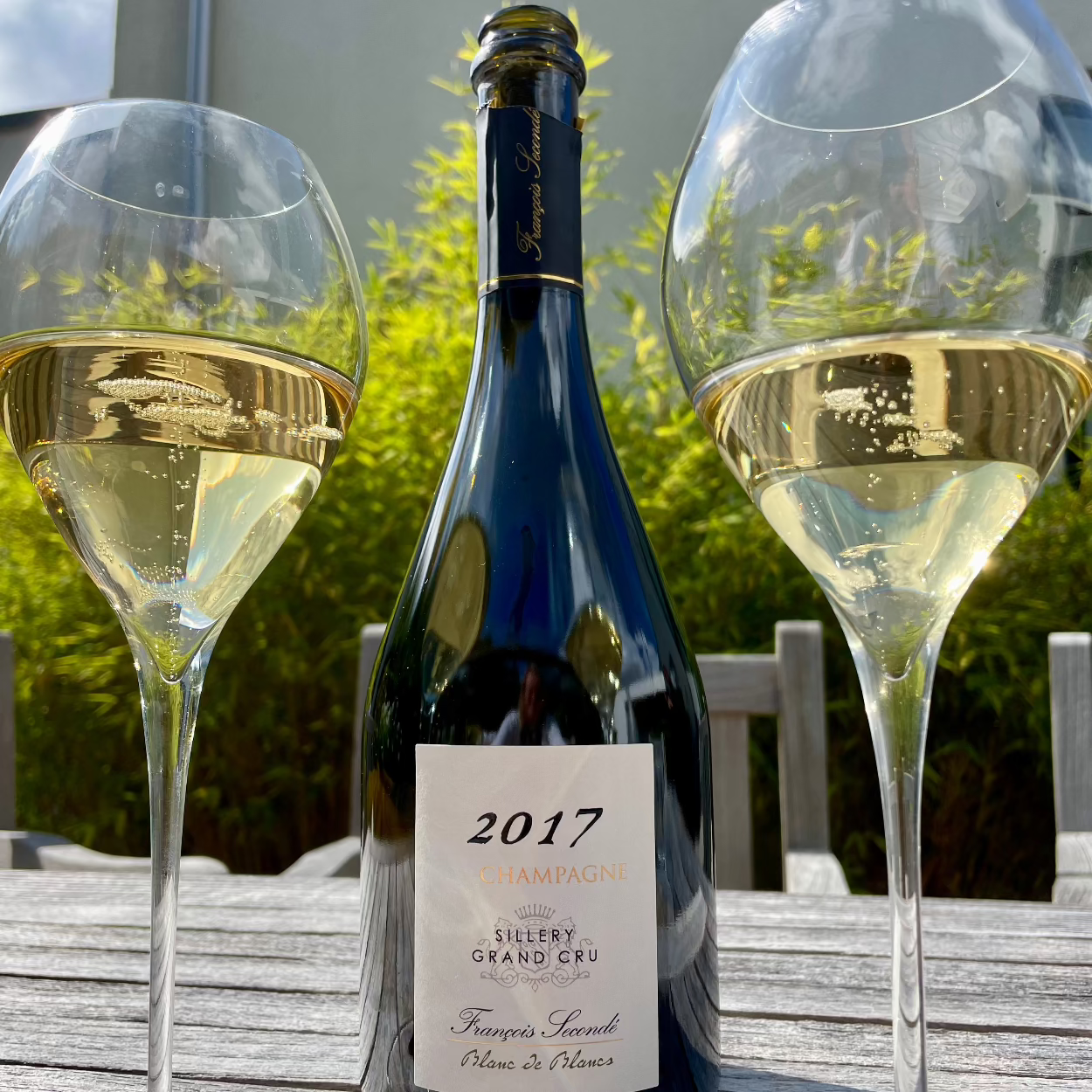 2 fyldte champagneglas på havebord og i midten 1 flaske årgangschampagne fra Francois Secondé, Blanc de Blancs år 2017, Sillery Grand Cru