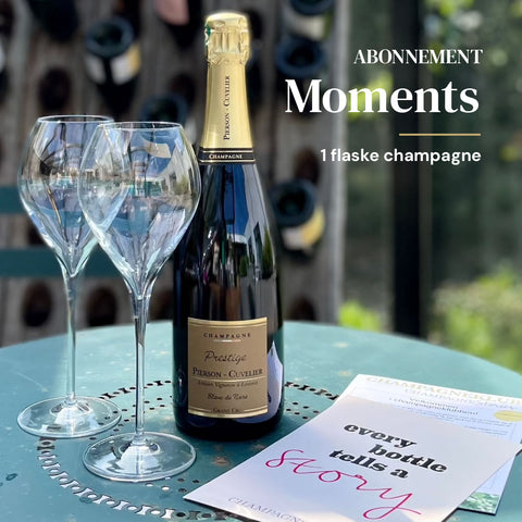 På bord står  2 champagneglas 41 cl, 1 flaske champagne Pierson-Cuvelier Prestige. Ved siden af ligger 1 klubflyer og 1 postkort med teksten "every bottle tells a stories - Champagne Stories"