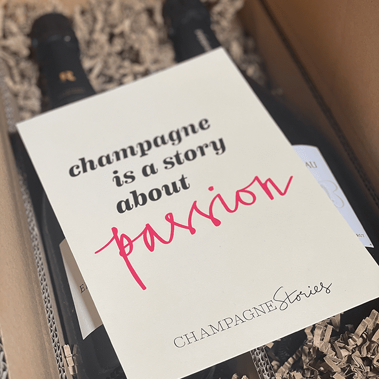 I en papkasse ligger 2 flasker champagne og over ligger 1 postkort med teksten "champagne is a story about passion - Champagne Stories"